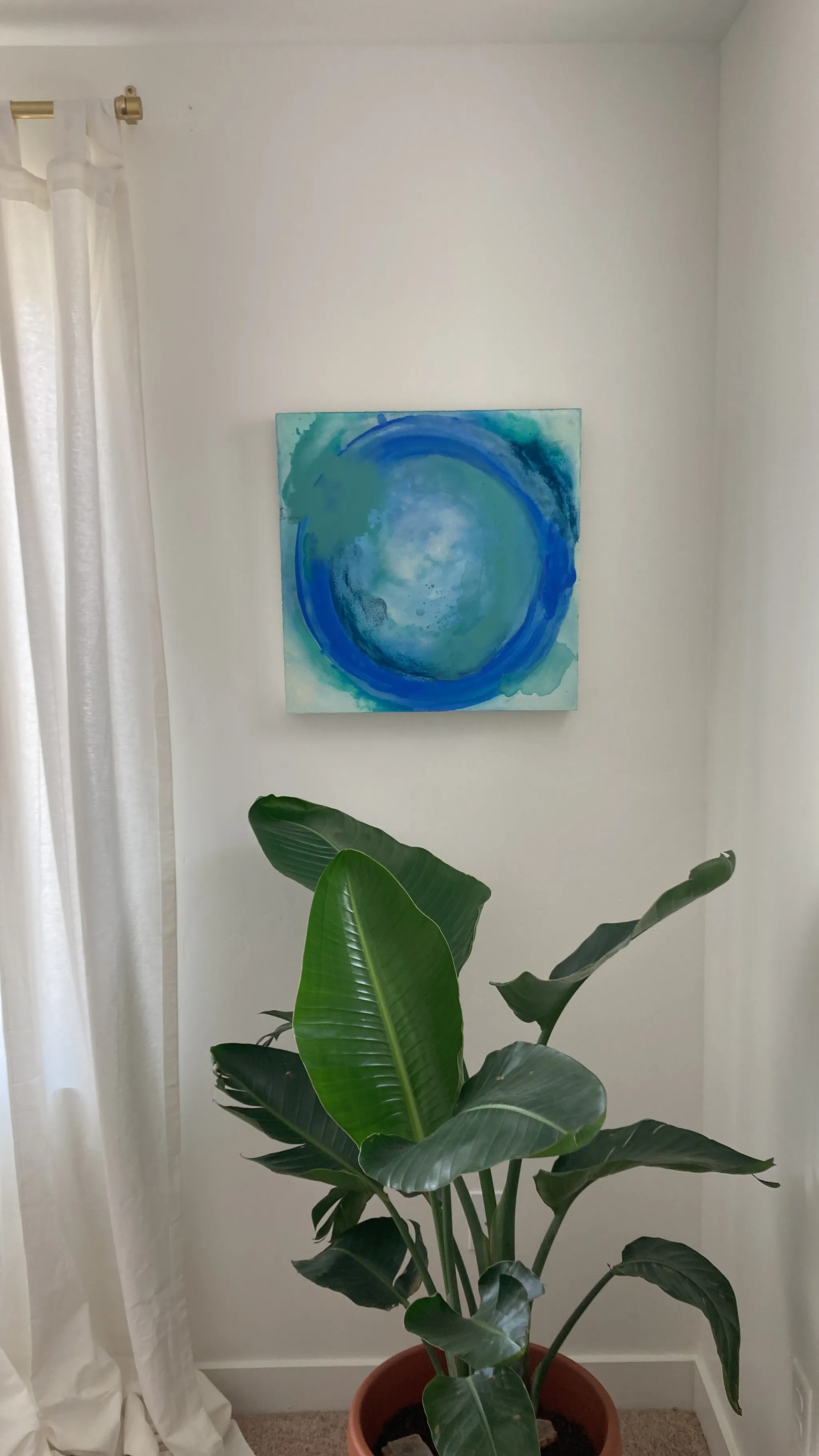 Abide hanging on a white wall beside a sheer white curtain, above a potted bird of paradise.