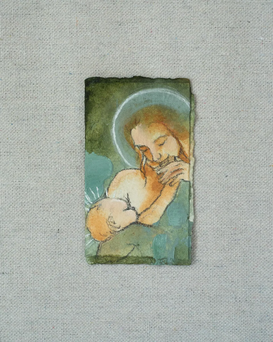 A small painting on torn-edged paper, laid on linen: a haloed mother with long auburn hair nursing her baby, in moss green and warm ochre.