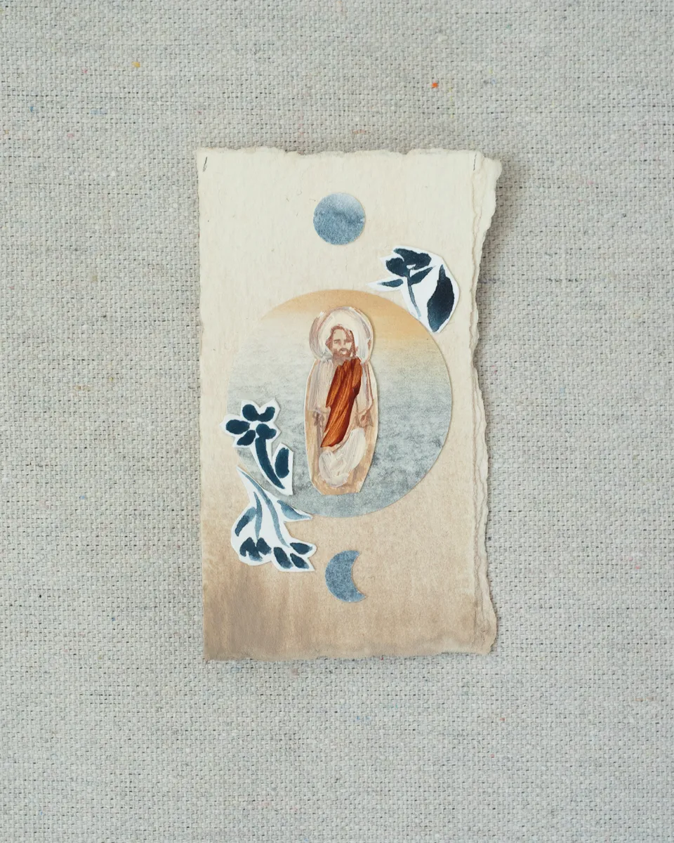 A small painting on torn-edged cream paper, laid on linen: a haloed figure of Christ in a red robe inside a pale blue circle, with a blue full moon above, a crescent below, and cut-paper indigo flowers.