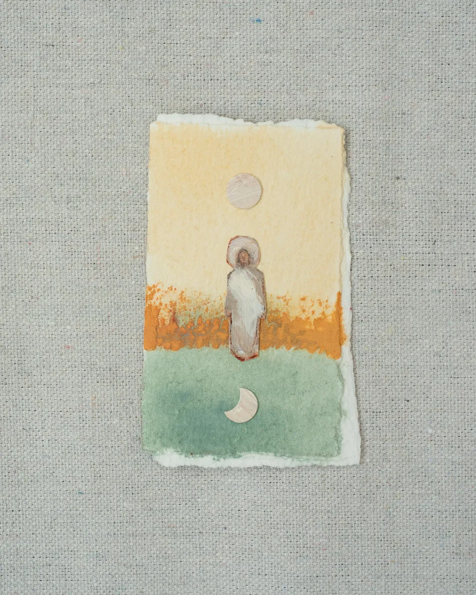 A small painting on torn-edged paper, laid on linen: a white-robed figure of Christ with a halo where pale yellow meets an orange band and a sage green field, with a full moon above and a crescent below.
