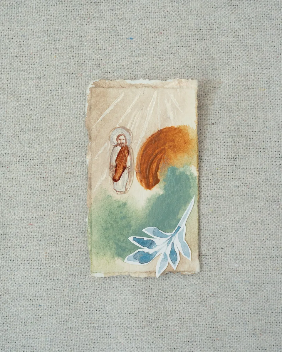 A small painting on torn-edged paper, laid on linen: a figure of Christ in a red-brown robe under painted rays, beside a sweep of burnt orange and a wash of teal, with a pale blue cut-paper sprig below.