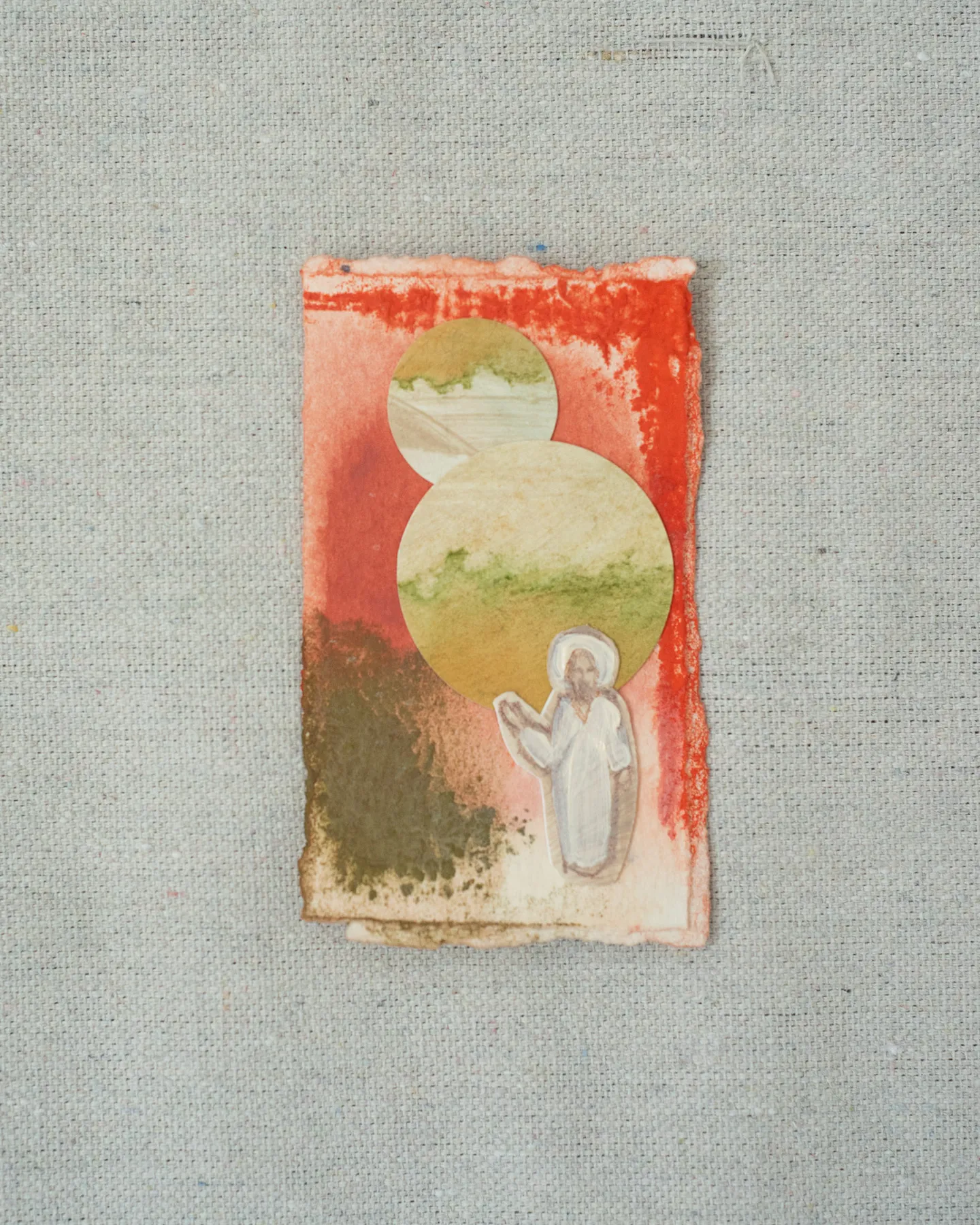 A small painting on torn-edged paper, laid on linen: two overlapping circles washed in green and cream on coral red and olive, with a white figure of Christ raising a hand beneath them.