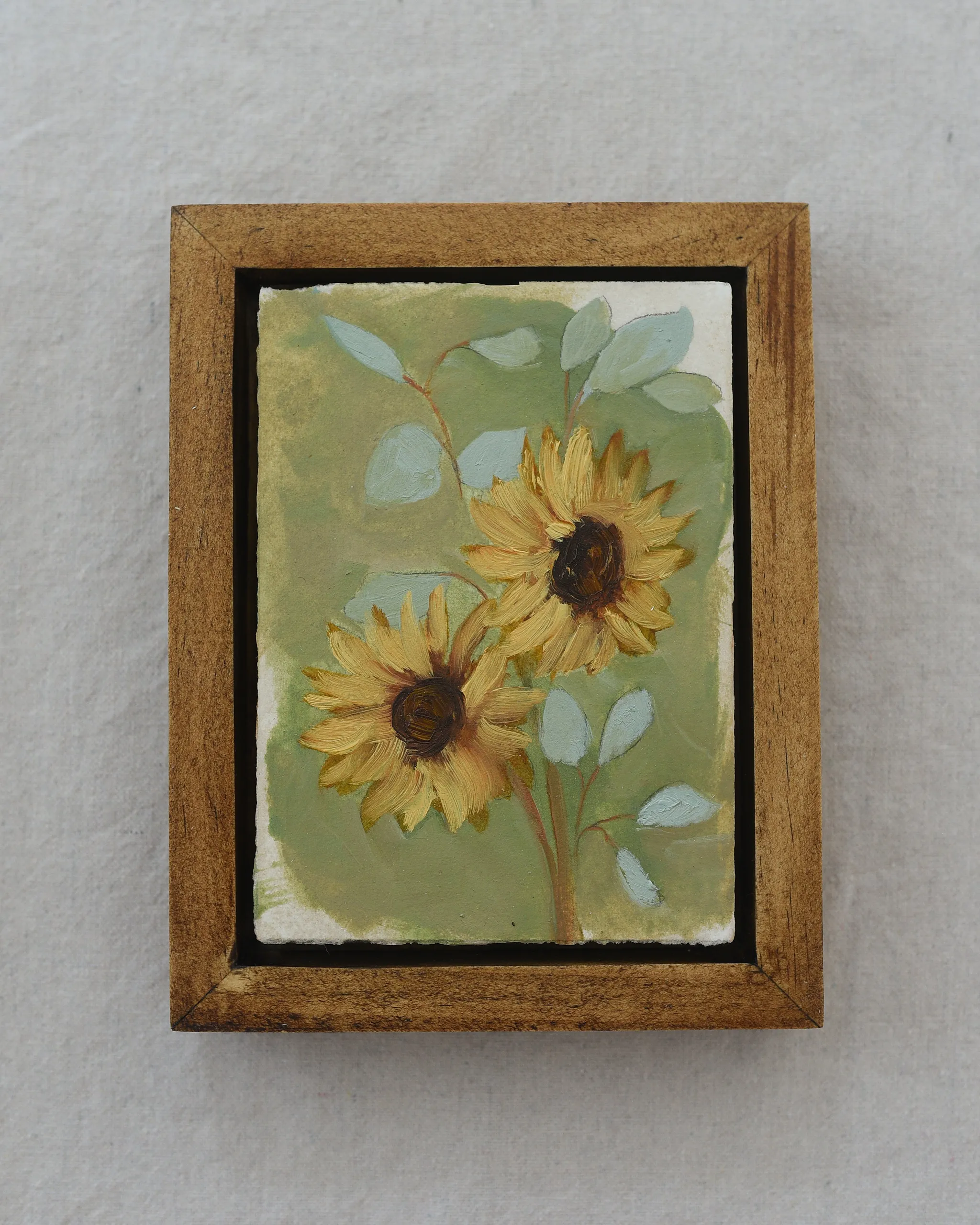 Three sunflowers radiating warmth against a light green backdrop, interwoven with delicate eucalyptus.
