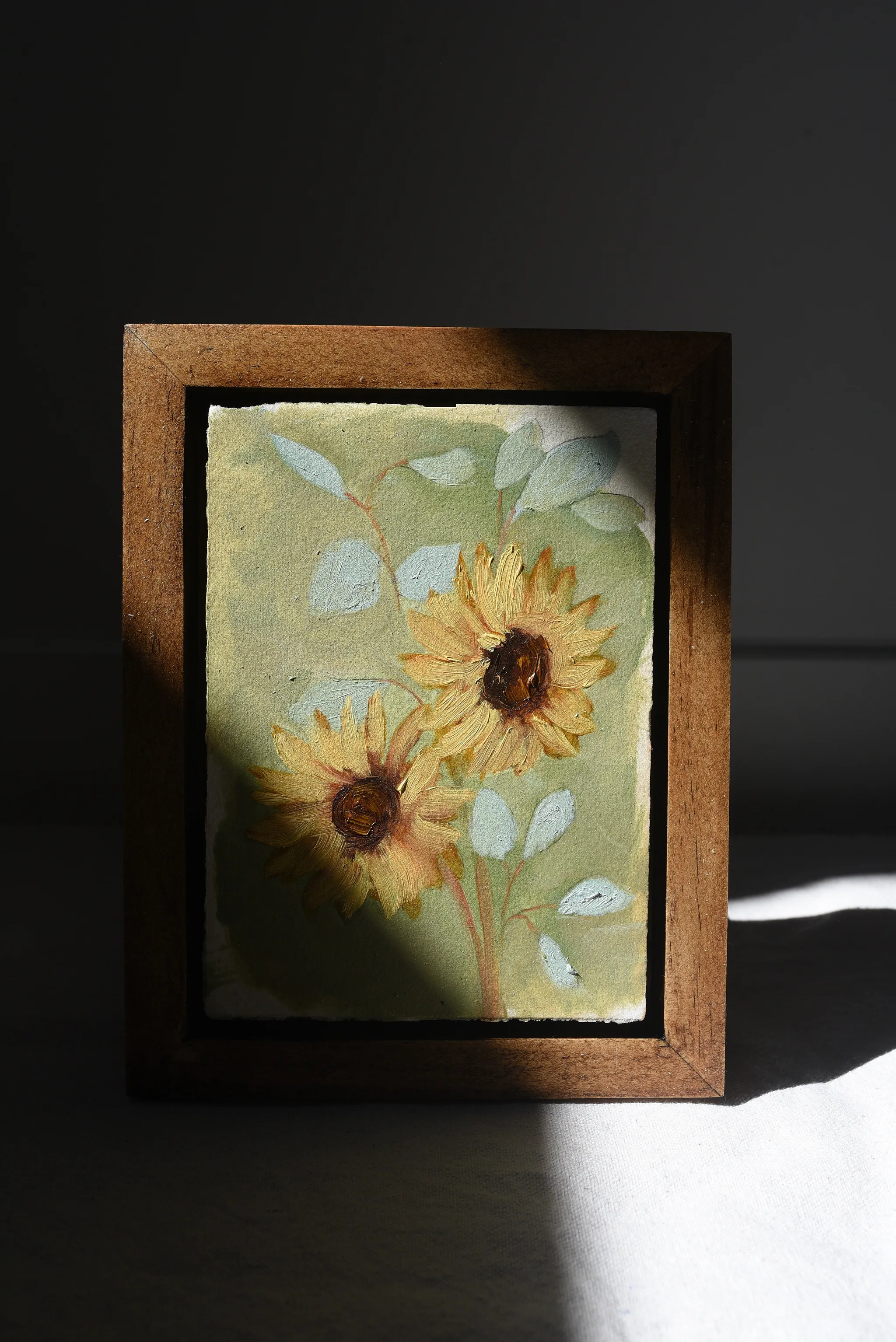 Harmony Bloom, view 3 of 12: three sunflowers radiating warmth against a light green backdrop, interwoven with delicate eucalyptus.