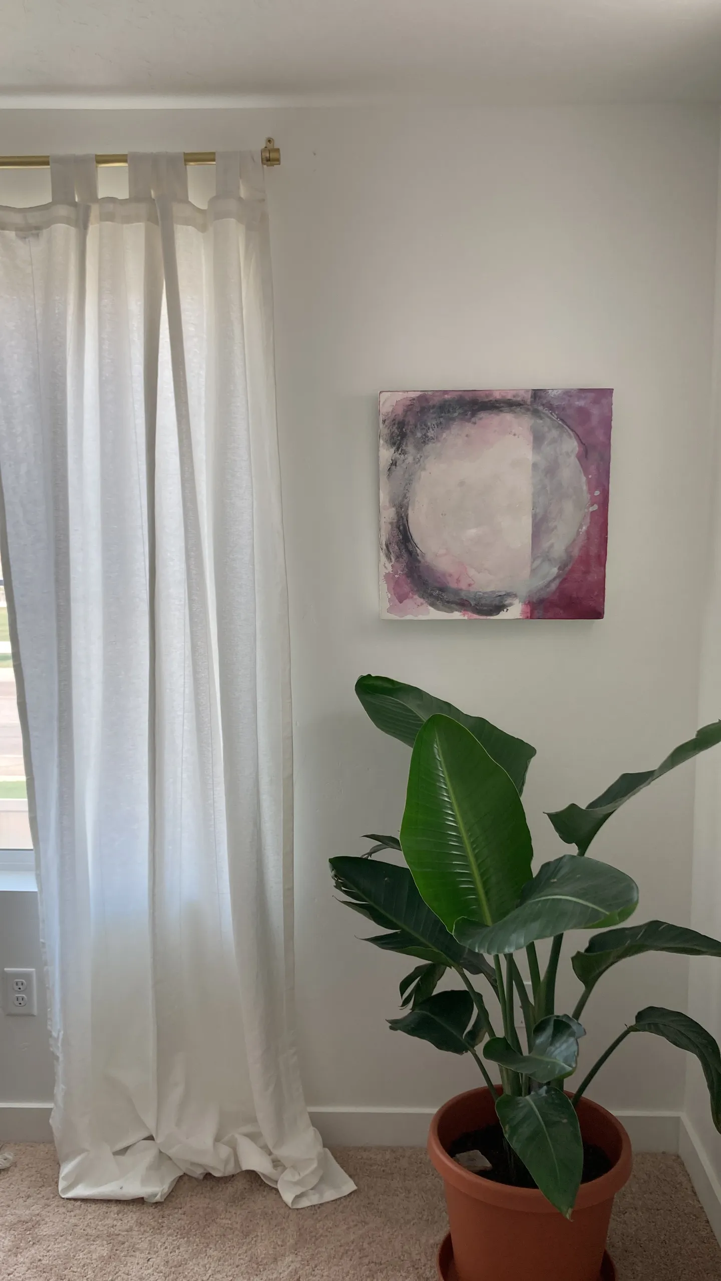 In Between hanging on a white wall beside a sheer white curtain, above a potted bird of paradise.