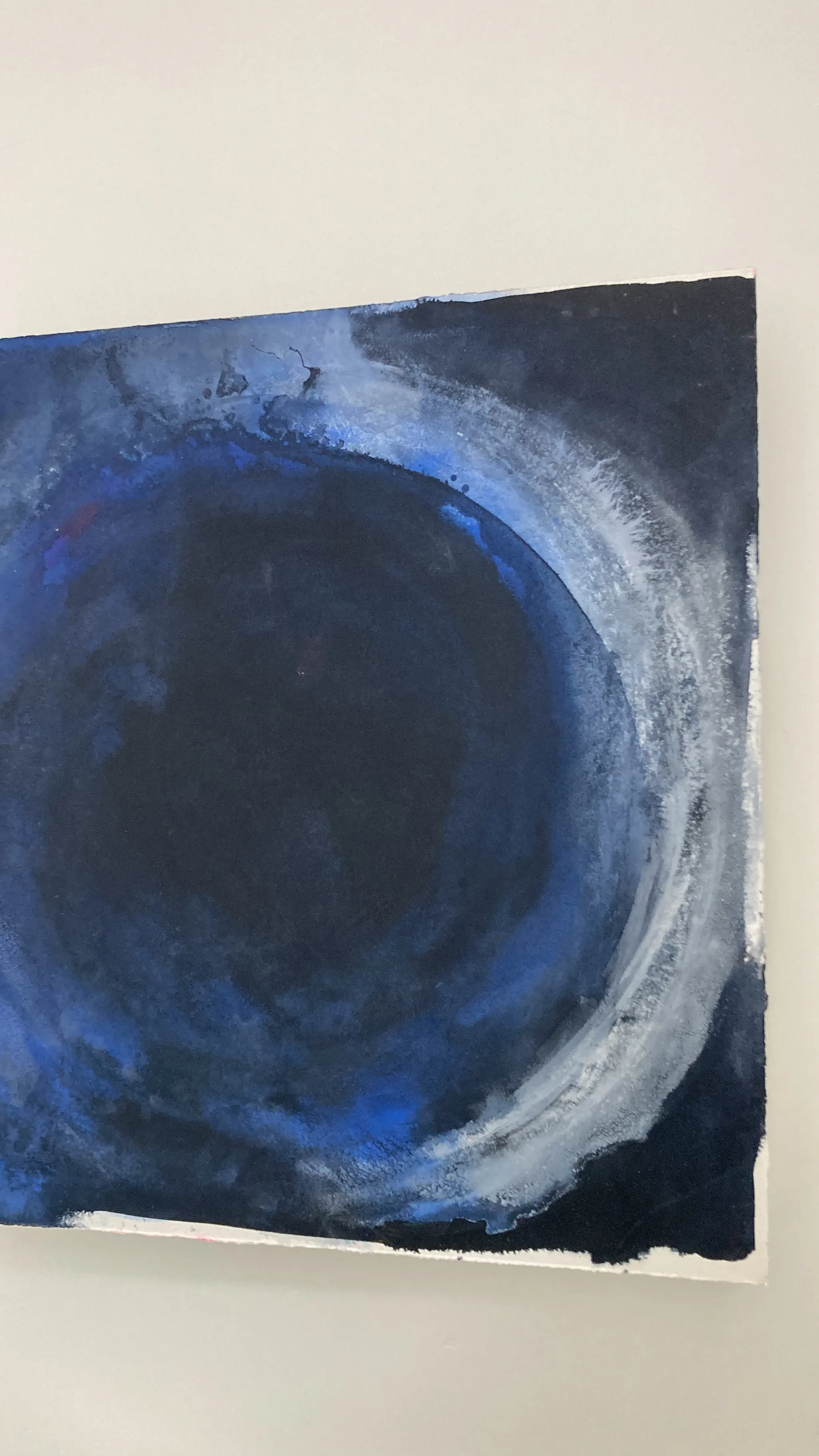 Overcome up close on the wall, a pale silver circle brushed through deep navy and blue.