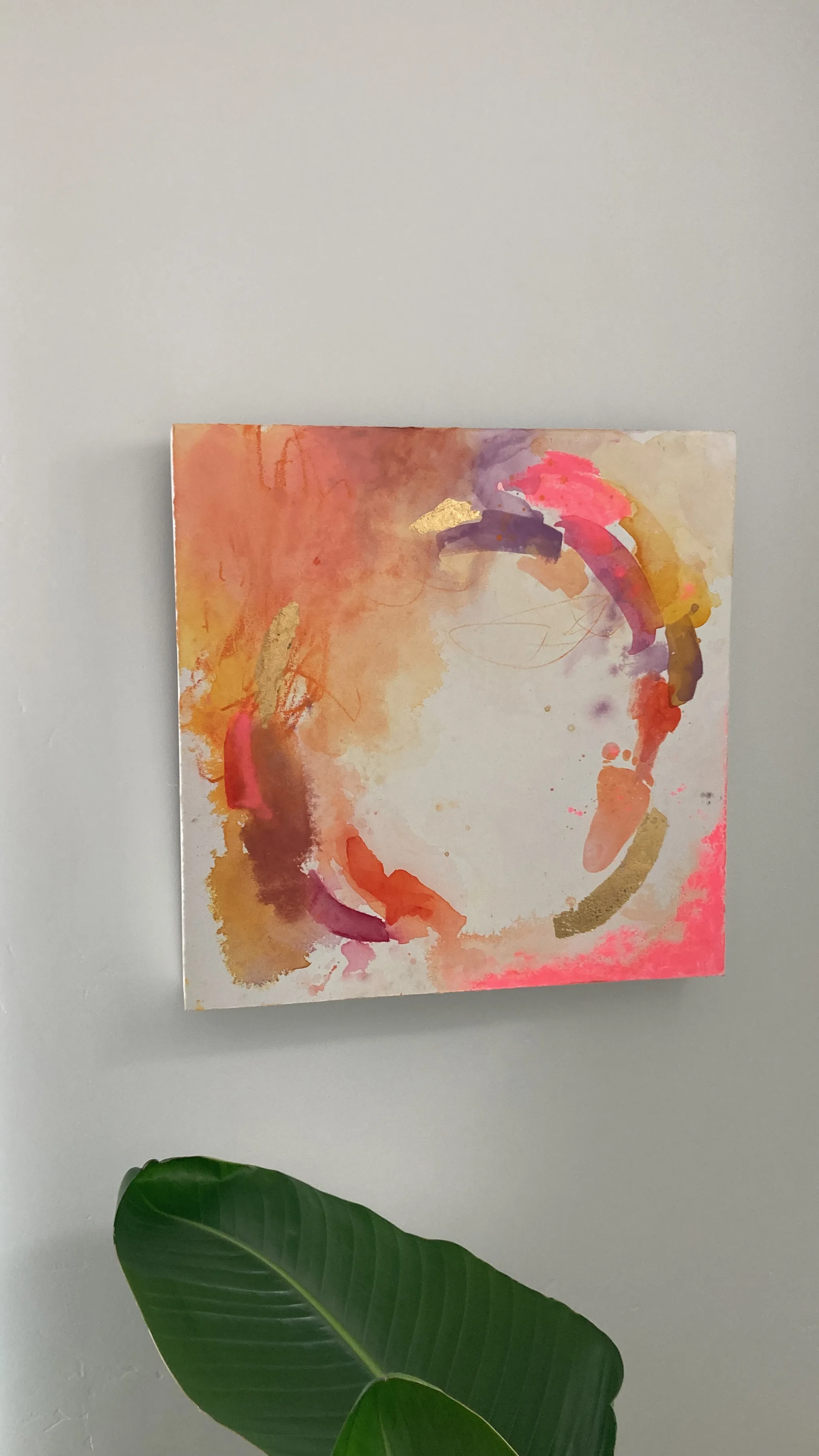Play seen from the side on the wall, pink and orange strokes circling a pale centre, a green leaf at the bottom edge.