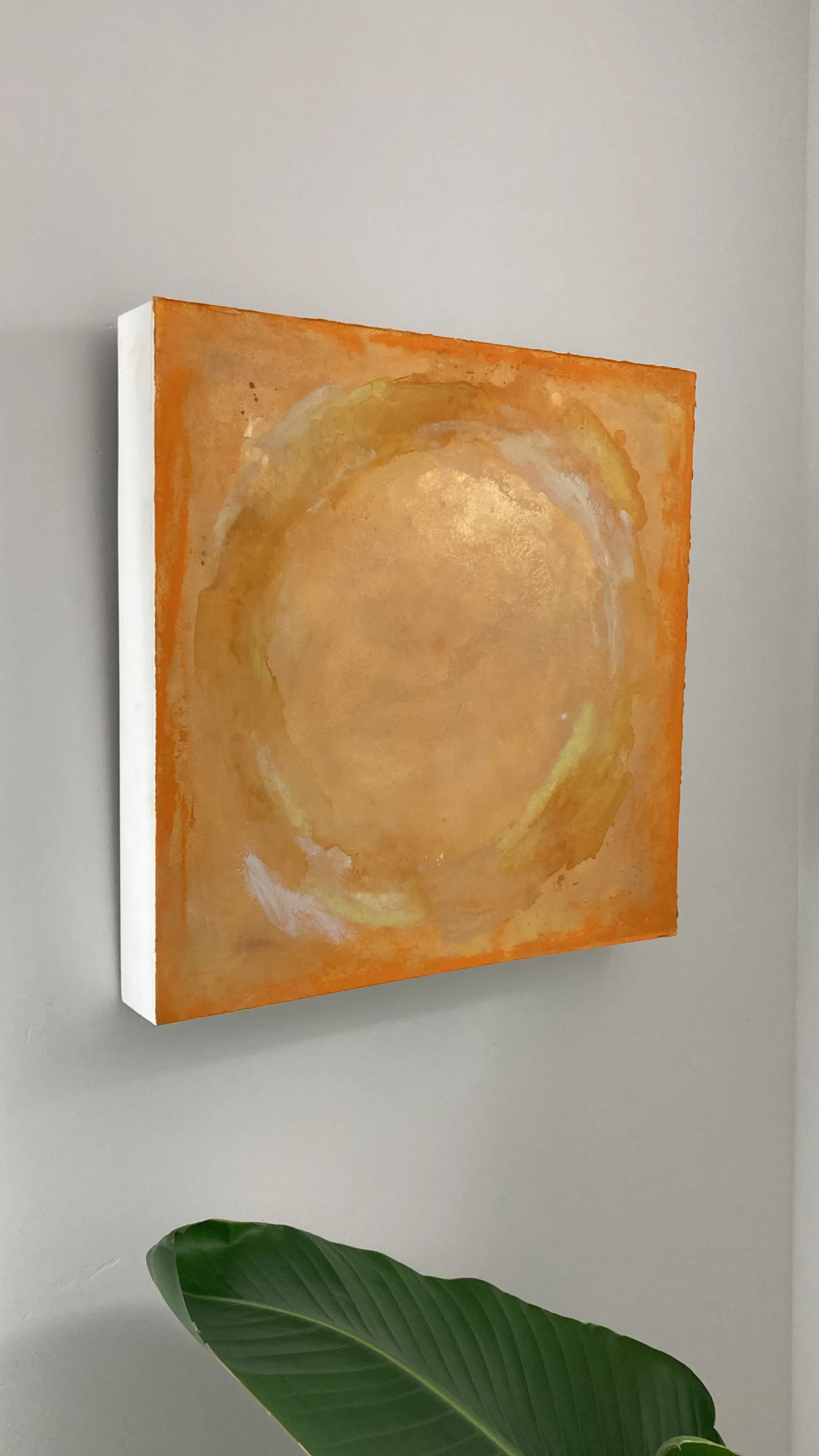 Unity seen from the side on the wall, a glowing yellow and ochre circle on a deep canvas, a green leaf at the bottom edge.