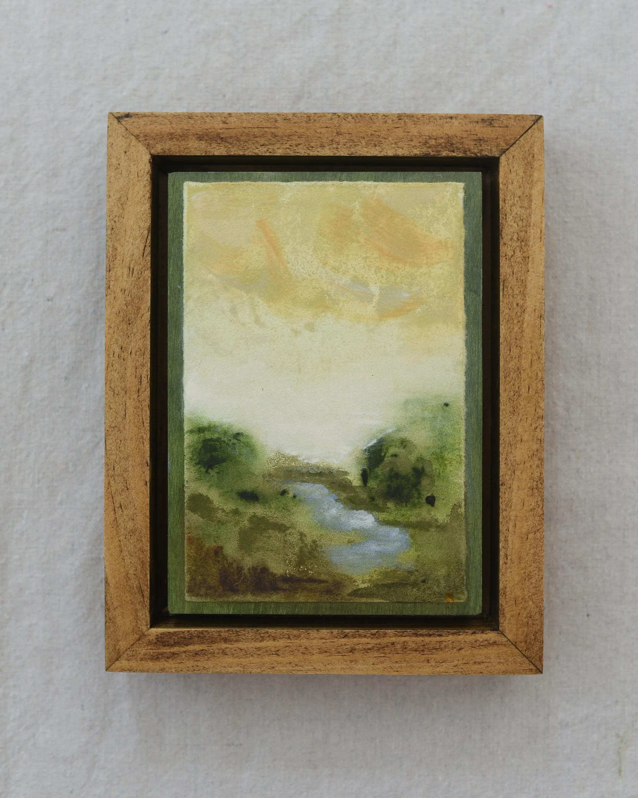 A moody scene of deep greens contrasted by a soft yellow sky, with a small stream gently wandering through the lush greenery.