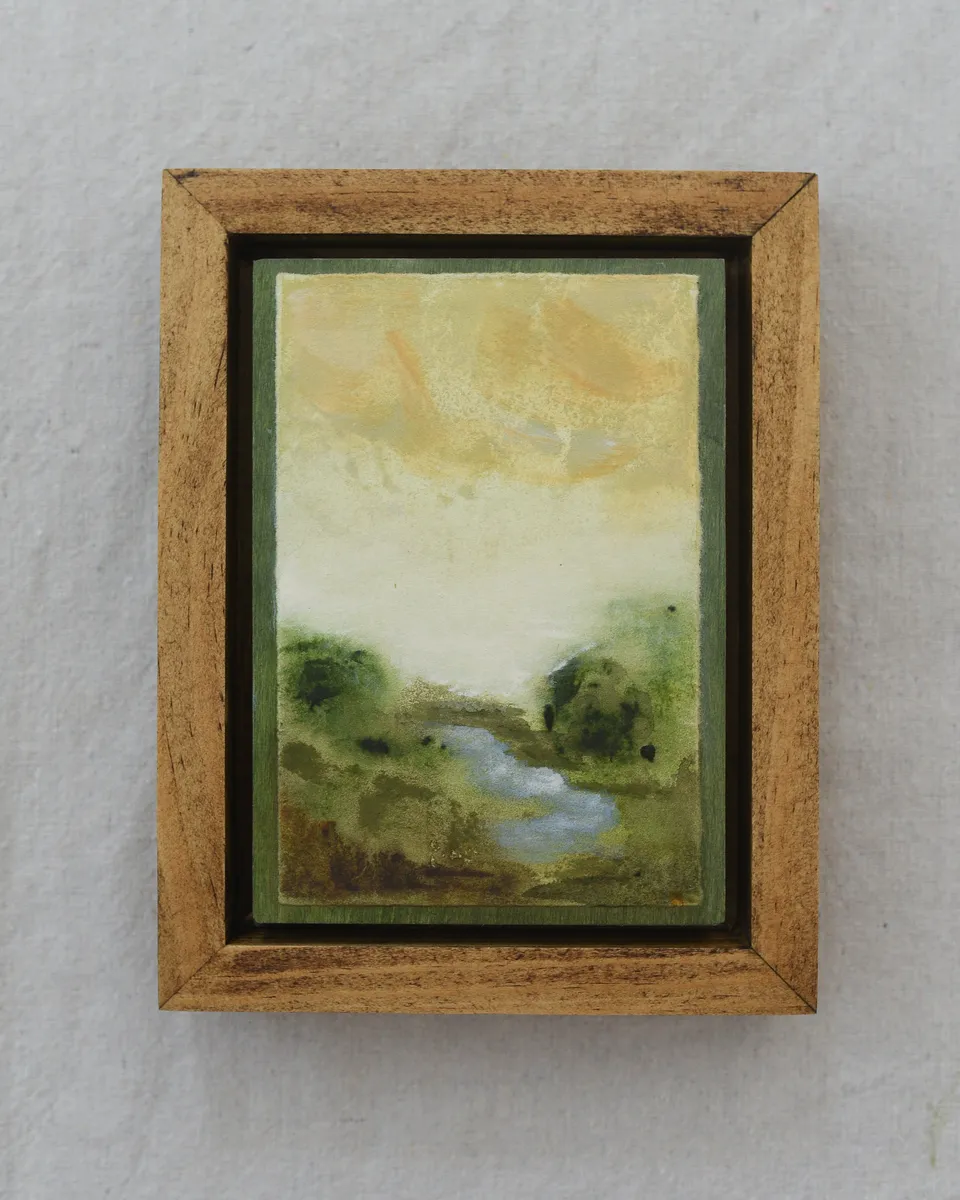 A moody scene of deep greens contrasted by a soft yellow sky, with a small stream gently wandering through the lush greenery.