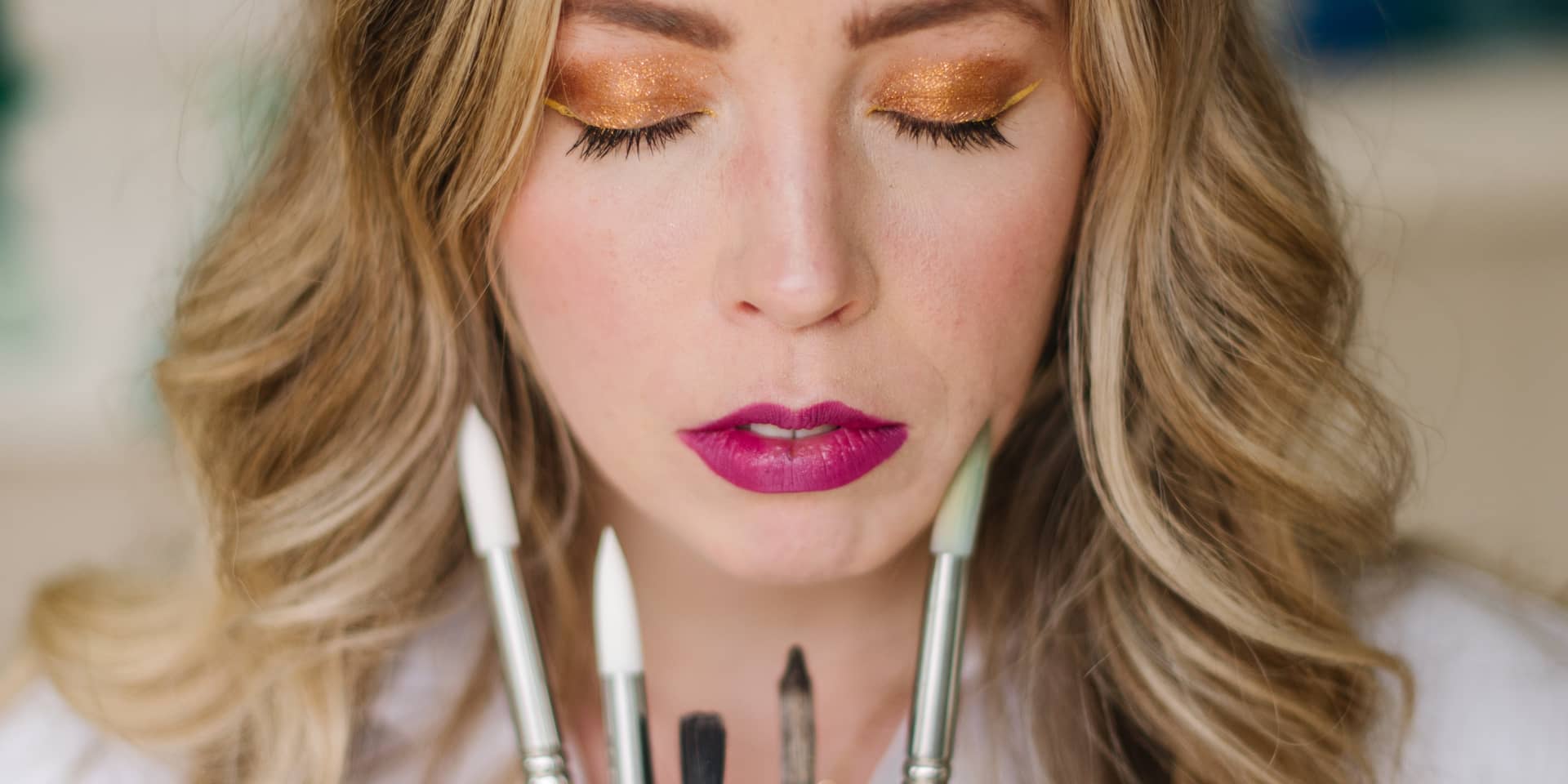 McKenna with her eyes closed, holding a fan of paintbrushes up in front of her face.