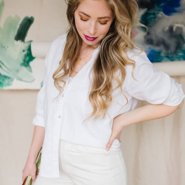 McKenna in a white shirt and trousers, standing in front of two large green and blue abstract paintings.