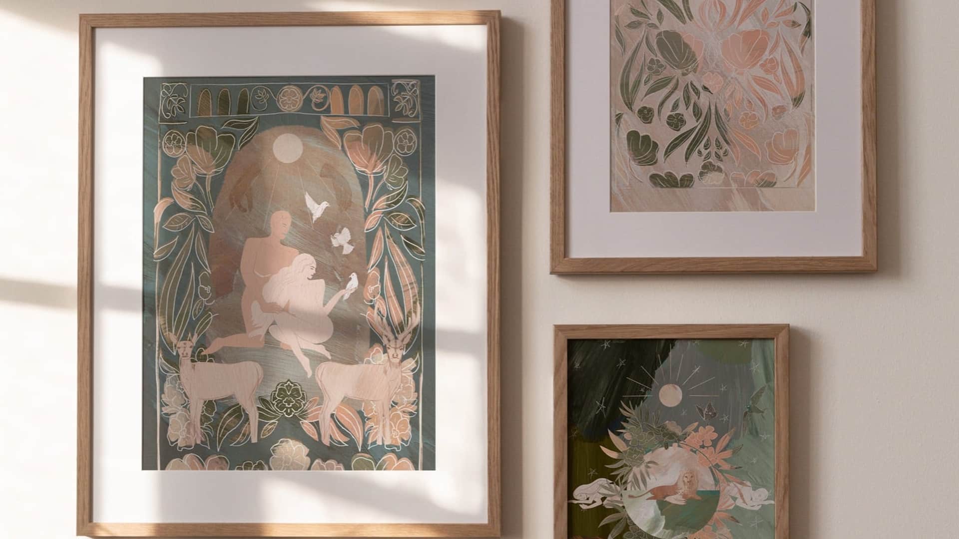 Simply Christ. Three framed prints on a pale wall in afternoon light: a green nativity with deer and tulips, a soft blush botanical, and a dark green scene of a figure under the moon.
