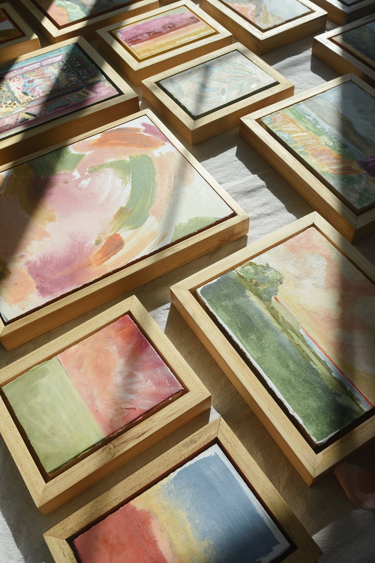 Two dozen of McKenna's small framed paintings laid out together on a pale floor, lit from one side by afternoon sun.
