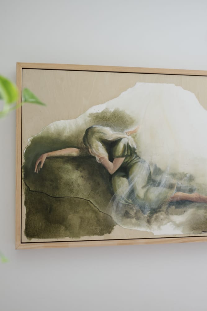 A Mother's Gethsemane framed in raw wood on a white wall, with a trailing green plant at one side and a deep terracotta curtain at the other.