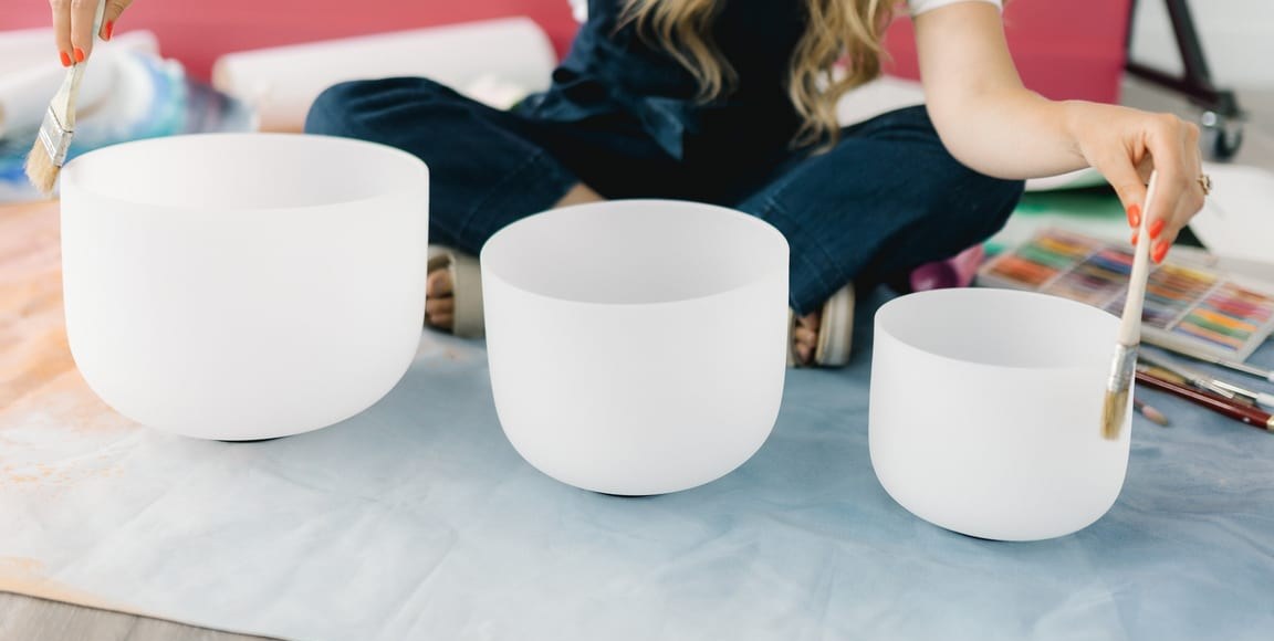 Close on her three singing bowls, a paintbrush resting in each hand at the edges.