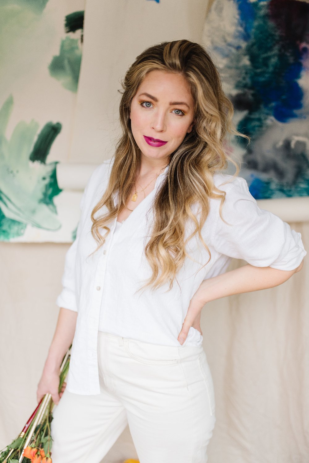 McKenna in her studio, holding flowers in front of her paintings.