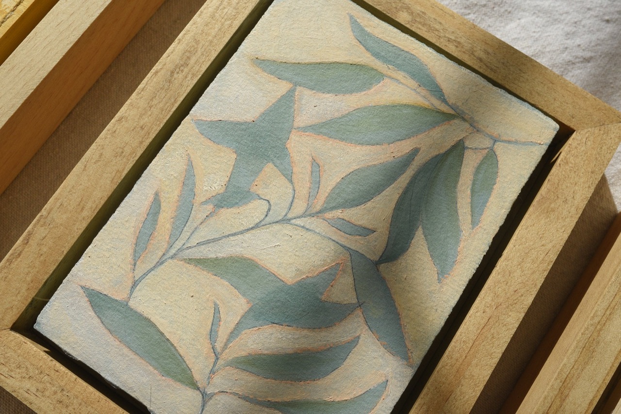 A close view of a leafy botanical painted in soft blue-green and cream, inside a raw wood float frame.
